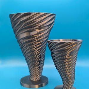 May include: Two gray, tornado-shaped decorative vases. The vases have a swirling, textured design and sit on circular bases. The larger vase is approximately 8 inches tall, and the smaller one is about 5 inches tall. The background is a solid blue.