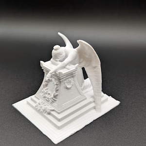 Puede incluir: Una escultura blanca de un ángel arrodillado sobre una base rectangular. El ángel tiene grandes alas y está cubierto por un pedestal decorado. La escultura está sobre un fondo oscuro.