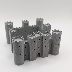 May include: A grey miniature castle model with multiple turrets and walls. The castle features cylindrical towers and rectangular walls with small square windows. The model is made of a solid, light grey material.