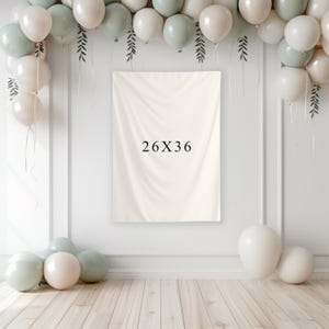 May include: A cream-colored backdrop with the text "26X36" is the focal point, surrounded by a balloon arch in white and sage green. The balloons are arranged with decorative greenery, creating a festive atmosphere. The backdrop measures 26 inches by 36 inches.