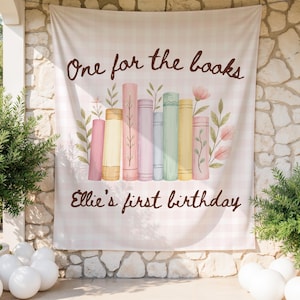 May include: A light pink and white checkered backdrop with the text "One for the books" and "Ellie's first birthday" in brown script. The backdrop features a watercolor illustration of colorful books and floral accents.