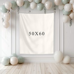 May include: A cream-colored backdrop with the text "50X60" is the focal point, surrounded by white, sage green, and cream-colored balloons. The backdrop is 50 inches by 60 inches. The balloons are arranged around the backdrop and on the floor, creating a festive atmosphere.