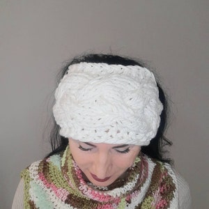 Peut inclure: Un bandeau blanc en crochet avec un motif tressé. Le bandeau est porté par une personne aux cheveux longs et foncés et une écharpe en crochet colorée.