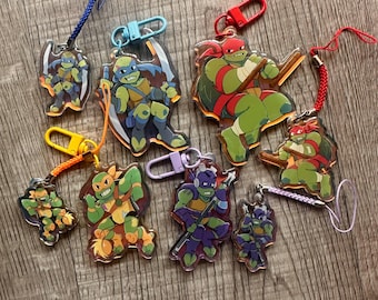 May include: A collection of acrylic keychains featuring the Teenage Mutant Ninja Turtles. Each keychain showcases a different turtle in action poses, with vibrant colors and attached lanyards and clasps for easy attachment.