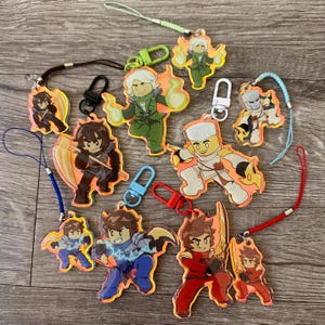 May include: A collection of colorful character keychains with various poses and designs. Each keychain features a different character with vibrant colors and attached lanyards or clasps for easy attachment. The keychains are made of a glossy material.