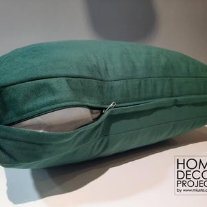 May include: A dark green velvet pillow with a zipper detail. The pillow is rectangular and has a soft, plush appearance. The zipper is partially open, revealing a light gray interior. Home decor project logo in the bottom right corner.