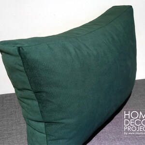 May include: A large, dark green decorative pillow with a triangular shape. The pillow is made of a soft, textured fabric and is designed for home decor. The pillow is placed on a gray surface.
