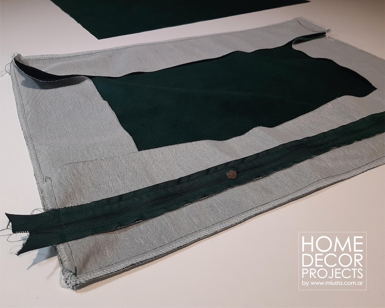 May include: A partially constructed dark green and gray fabric project. The project features a dark green zipper and a dark green fabric insert. The fabric is laid out on a white surface. The image includes the text "HOME DECOR PROJECTS by www.miusta.com.ar".