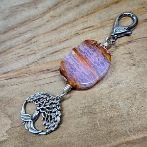 May include: A silver tree of life charm with a pink and brown agate stone attached to a silver key chain.