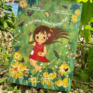May include: A book cover with a green background and a girl with brown hair and a red dress raising butterflies. The title of the book is "A Girl Who Raises Butterflies".