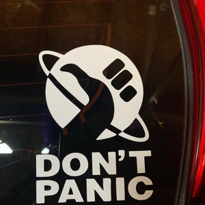May include: A white sticker on a car window with a black silhouette of a hand giving a thumbs up inside a circle with a ring around it. The text "DON'T PANIC" is below the circle.