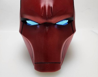 May include: A red plastic mask with a textured surface and blue glowing eyes. The mask is designed to resemble a superhero's head.