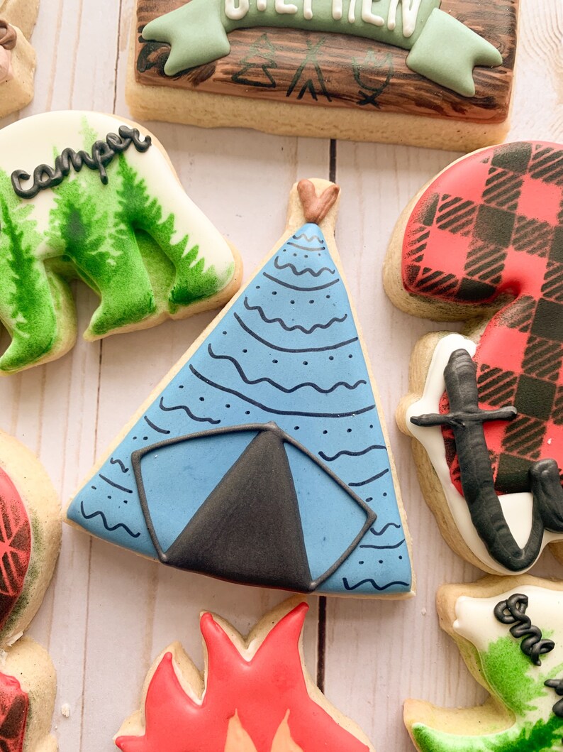 Puede incluir: Una galleta de az&uacute;car decorada en azul y negro con forma de tienda de campa&ntilde;a. La tienda de campa&ntilde;a tiene una solapa negra y puntos blancos y l&iacute;neas onduladas en la tela azul.