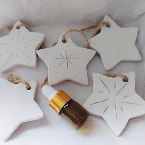 May include: Five white star-shaped decorations with textured patterns and twine loops. A small brown glass bottle with a gold cap is also present. The items are likely for decorative or aromatherapy purposes.