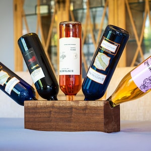 May include: A wooden wine bottle holder with five wine bottles in various colours and labels. The bottles are arranged in a circular pattern, with the necks of the bottles pointing outwards.