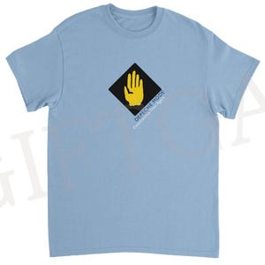 Peut inclure: T-shirt bleu clair avec un motif de main jaune dans un losange noir. Le texte "DEPECHE MODE Construction Time Again" est imprimé en dessous. Le t-shirt a des manches courtes et un col rond.