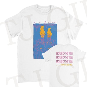 May include: White t-shirt with a blue graphic of two figures and the text "Barry Adamson". The back of the shirt displays the text "BECAUSE OF THIS THING... THAT'S IN ME." in pink. A relaxed fit, unisex tee.