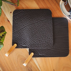 Könnte beinhalten: Zwei schwarze Topfhandschuhe aus Leder mit braunen Ledergriffen. Die Topfhandschuhe haben eine strukturierte Oberfläche.