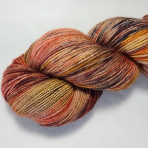 May include: A skein of yarn in a blend of warm colors, including shades of orange, brown, and yellow. The yarn is tightly wound, showing the texture and individual strands. Ideal for knitting or crocheting projects.