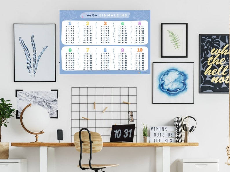 May include: A blue and white multiplication chart poster with the title "Das kleine Einmaleins" and numbers 1 through 10. The poster is hanging on a white wall in a home office setting.