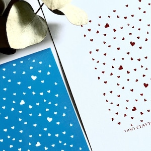 Puede incluir: Un esténcil azul con un patrón de corazones blancos y el texto "TIDO CLAYTOOLS". Junto a él, un papel blanco con un patrón de corazones rojos y el mismo texto. La imagen está sobre una superficie blanca.
