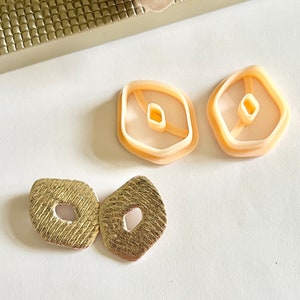 Peut inclure: Deux paires de boucles d'oreilles, une paire est dorée et l'autre est pêche. Les boucles d'oreilles dorées sont texturées et ont un trou rond au centre. Les boucles d'oreilles pêche sont lisses et ont un trou rond au centre.