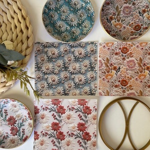 May include: Six round coasters with floral patterns. The coasters are made of ceramic and have a gold rim. The patterns include blue and white daisies, red and white daisies, and red and orange flowers. There is also a gold metal coaster with a circular design.