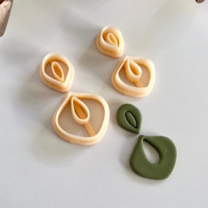 Może przedstawiać: Zestaw czterech kolczyków z polimerowej gliny w dwóch różnych stylach. Dwa kolczyki są w kolorze brzoskwiniowym i mają warstwowy kształt łzy. Dwa pozostałe kolczyki są ciemnozielone i mają kształt łzy z otworem w środku.