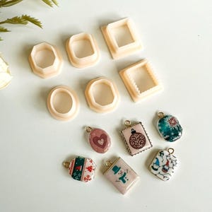 Puede incluir: Una colección de cortadores de arcilla polimérica rosa claro en varias formas, incluyendo óvalos, rectángulos y octágonos. Debajo, varios dijes de resina con temática navideña con lazos dorados, con diseños como un muñeco de nieve y patrones festivos.