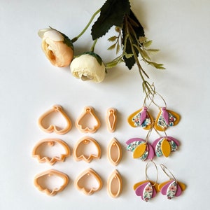 May include: A set of polymer clay earring making supplies. The set includes three different sizes of flower-shaped cutters, a leaf-shaped cutter, and two pairs of earrings made with floral patterned polymer clay.