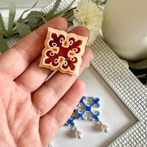 May include: A pair of ceramic earrings with a blue and white geometric design. The earrings have a pearl drop pendant.