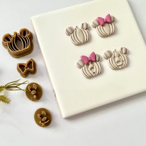 Könnte beinhalten: Ein Set aus braunen Polymer Clay-Formen zum Herstellen von Kürbis-Ohrringen. Die Formen zeigen einen Kürbis mit einem Gesicht und einer Schleife oben. Es gibt auch zwei kleinere Formen, eine mit einer Schleife und eine mit einem Gesicht.