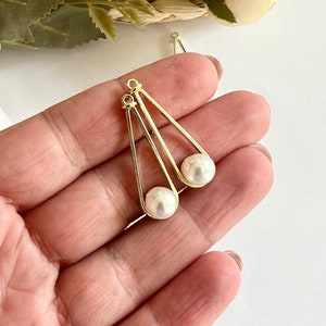 以下が含まれることがあります： 三角形の形状をした金色のイヤリング金具のペア。各金具にパールが取り付けられています。