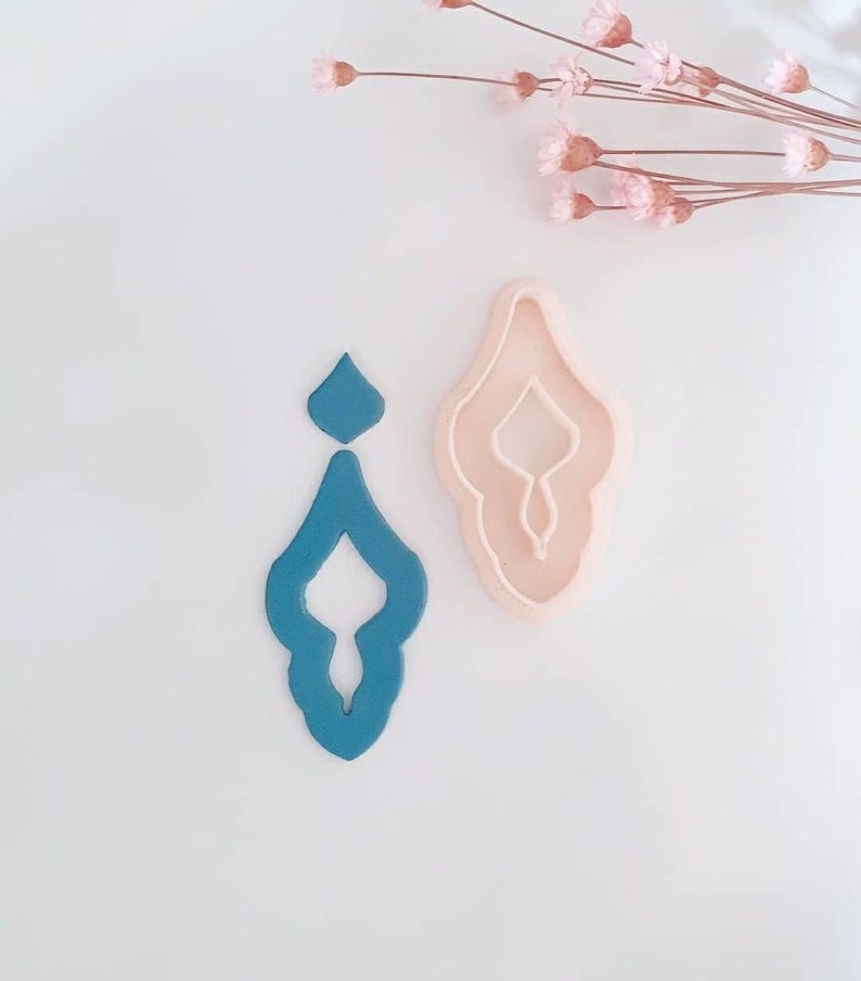 May include: Two cookie cutters, one teal blue and one light pink, shaped like a stylized teardrop with an intricate design.