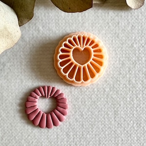 Peut inclure: Deux emportes-pièces, l'un rose et l'autre pêche, en forme de fleur avec un cœur au centre.