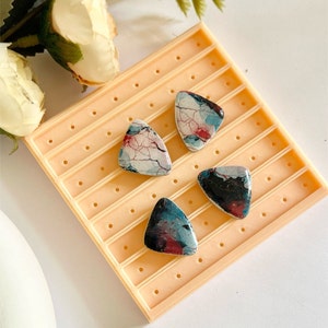Puede incluir: Tres pendientes triangulares de resina con patrones de mármol abstractos en tonos de azul, rojo y blanco. Los pendientes se muestran en un expositor de pendientes de color naranja claro.