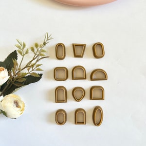 Könnte beinhalten: Ein Set mit 12 goldfarbenen Ausstechern in verschiedenen Formen, darunter Kreise, Ovale, Bögen und eine Träne. Die Ausstecher sind in drei Reihen auf einer weißen Oberfläche angeordnet.