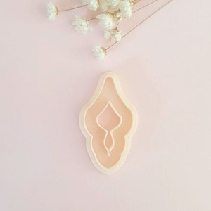 May include: A light pink plastic cookie cutter shaped like a female reproductive organ.