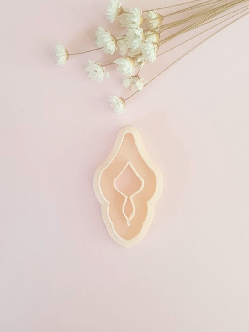 May include: A light pink plastic cookie cutter shaped like a female reproductive organ.