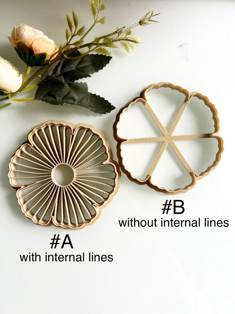 May include: Two wooden flower-shaped cookie cutters. One has internal lines, labeled "#A with internal lines." The other, labeled "#B without internal lines," lacks internal lines. Artificial flowers and leaves are in the background.