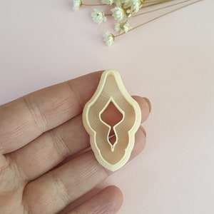 May include: A light beige plastic cookie cutter shaped like a female reproductive organ.