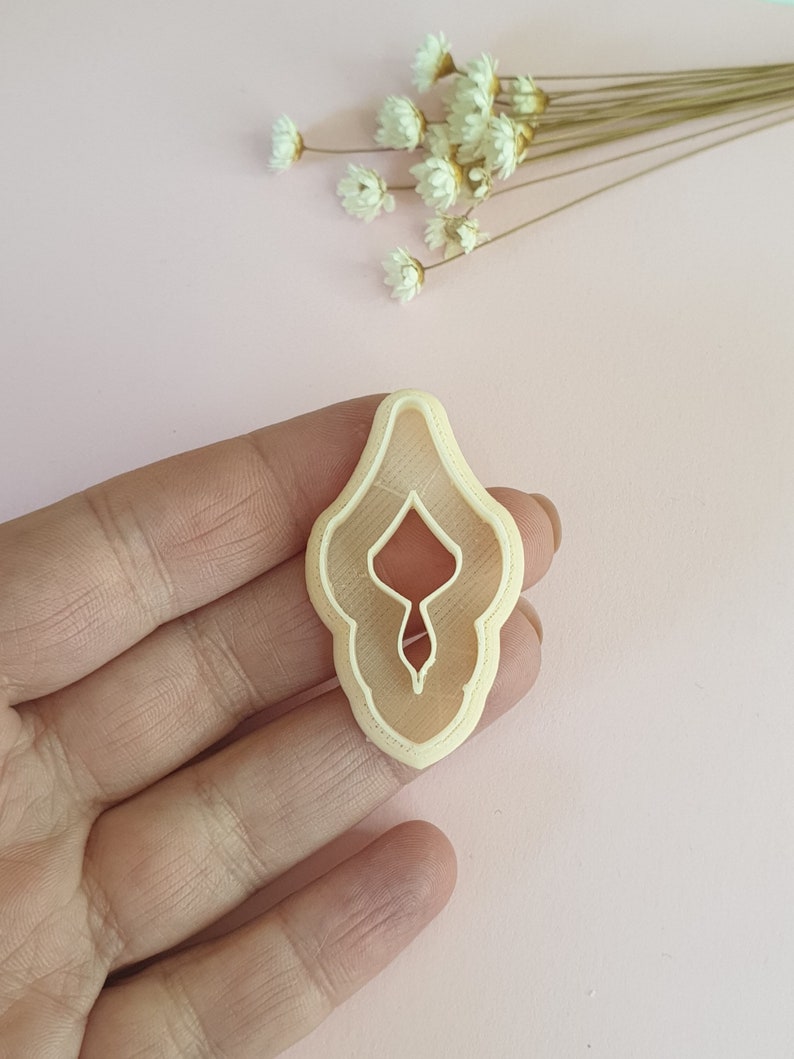 May include: A light beige plastic cookie cutter shaped like a female reproductive organ.