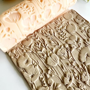 Pode incluir: Um rolo de massa cor de pêssego claro com um design floral, ao lado de um bloco retangular com o mesmo padrão em relevo. O padrão inclui flores e folhas. O rolo é cilíndrico e o bloco é retangular.