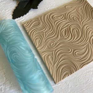 Peut inclure: Un rouleau à pâtisserie bleu et un tapis en silicone texturé brun pour la cuisson et la décoration de gâteaux et de pâtisseries. Le rouleau à pâtisserie et le tapis ont un motif en spirale.