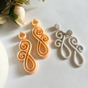 May include: Two pairs of earrings with a swirl design. One pair is a light peach colour and the other pair is a light grey colour.