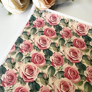 May include: A floral pattern featuring watercolor roses in shades of pink and red, with green leaves, set against a cream-colored background. The roses are in full bloom, creating a vintage aesthetic. The image is of a paper or fabric with a repeating floral design.