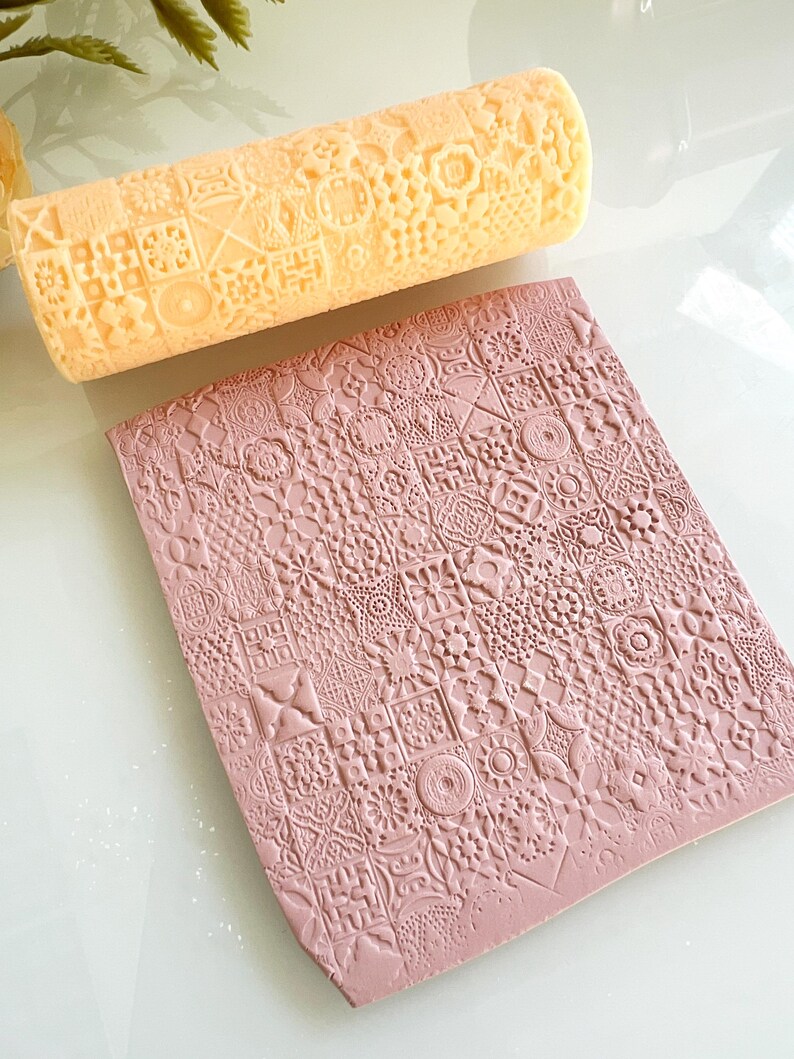 Pu&ograve; includere: Un mattarello a motivi giallo chiaro e un tappetino rosa strutturato. Il mattarello presenta un motivo ripetuto di quadrati, fiori e forme geometriche. Il tappetino rosa presenta un motivo ripetuto simile di quadrati e motivi floreali.