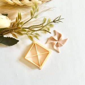 May include: A light brown plastic square cookie cutter with four sections and a pink plastic pinwheel.