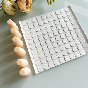 May include: A square sheet of white adhesive circular pads arranged in a grid pattern, accompanied by six individual beige tapered conical stoppers. The stoppers are smooth and solid in appearance, while the adhesive sheet contains many small circles.