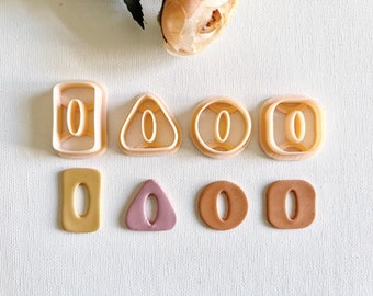 Op de afbeelding: Set van zes koekjesvormen in de vorm van een rechthoek, driehoek en cirkel. Elke vorm heeft een letter "O" uitgesneden in het midden. De vormen worden getoond naast zes koekjes die met dezelfde vormen en letter zijn uitgesneden.